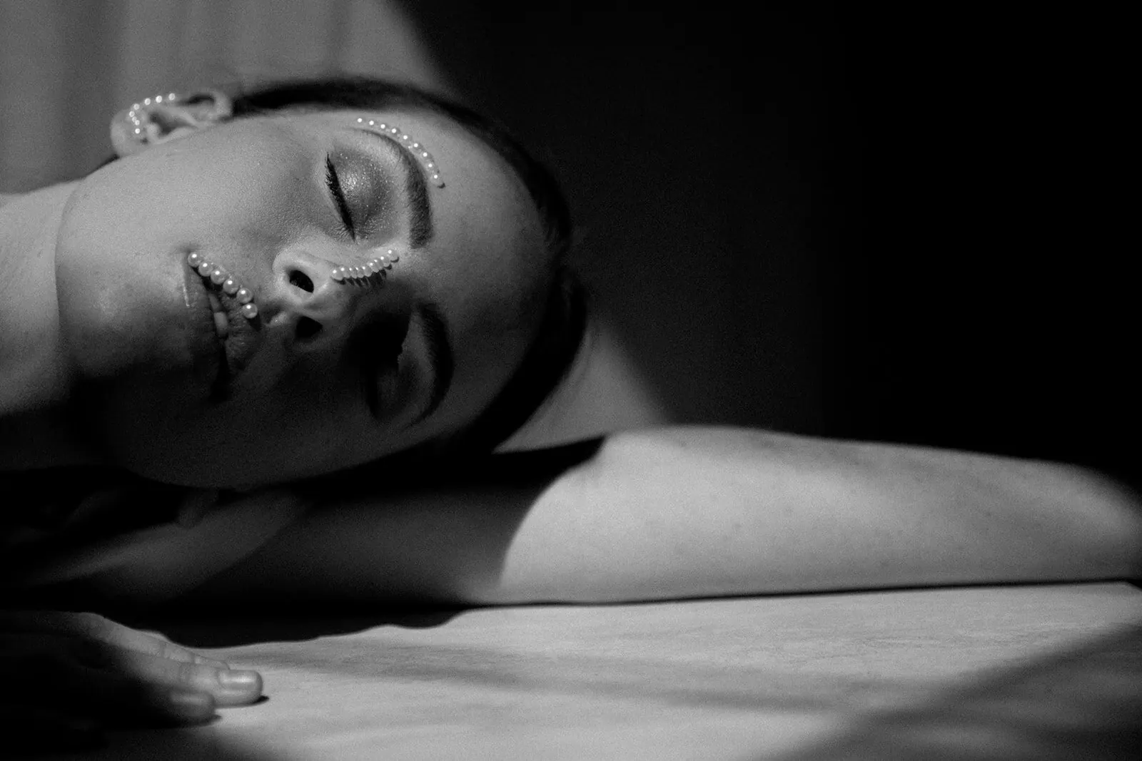 Black-and-white portrait of a woman resting her head on a table, pearls along her cheek