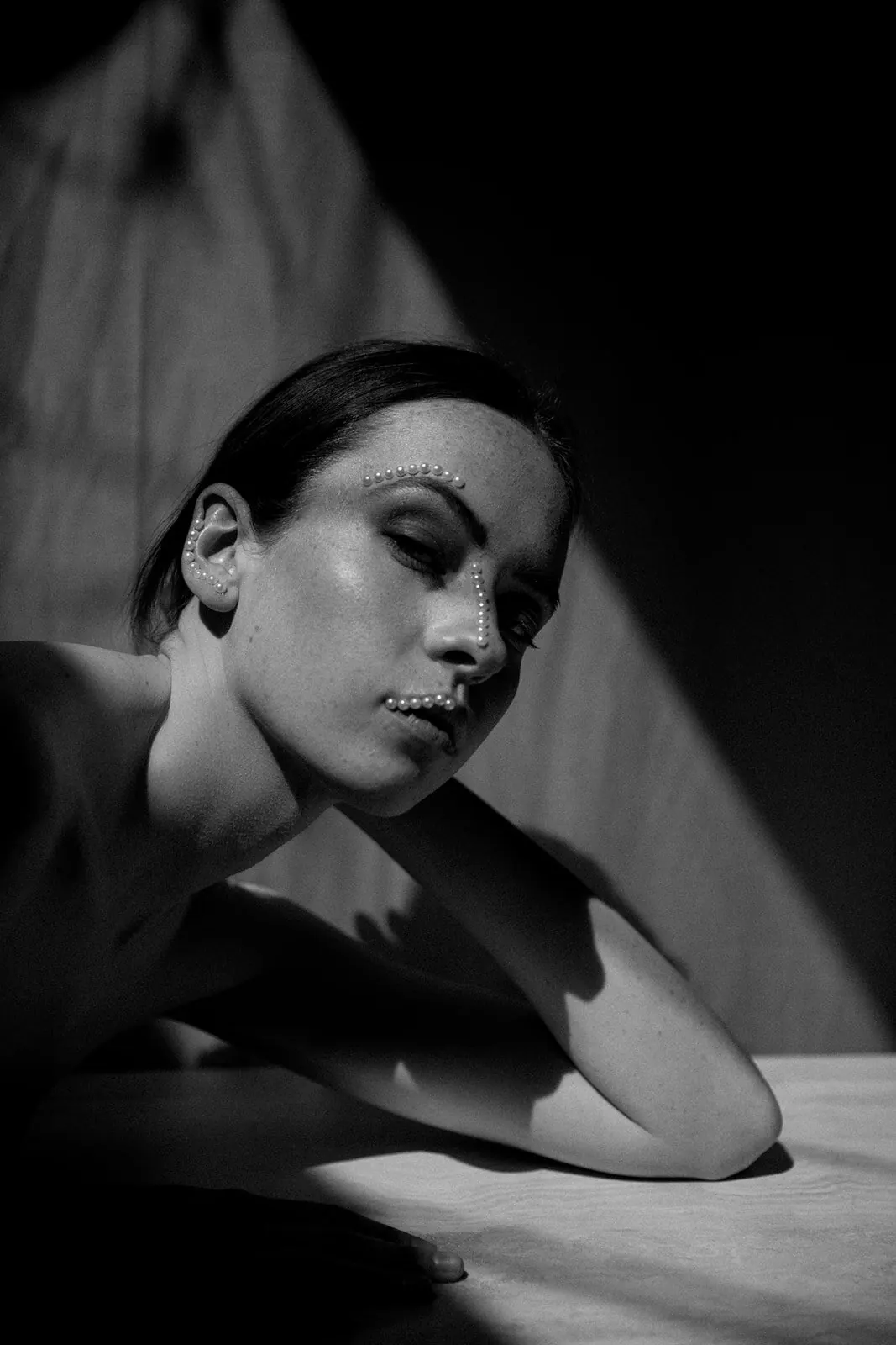 Black-and-white portrait of a woman leaning on a table in dramatic window light