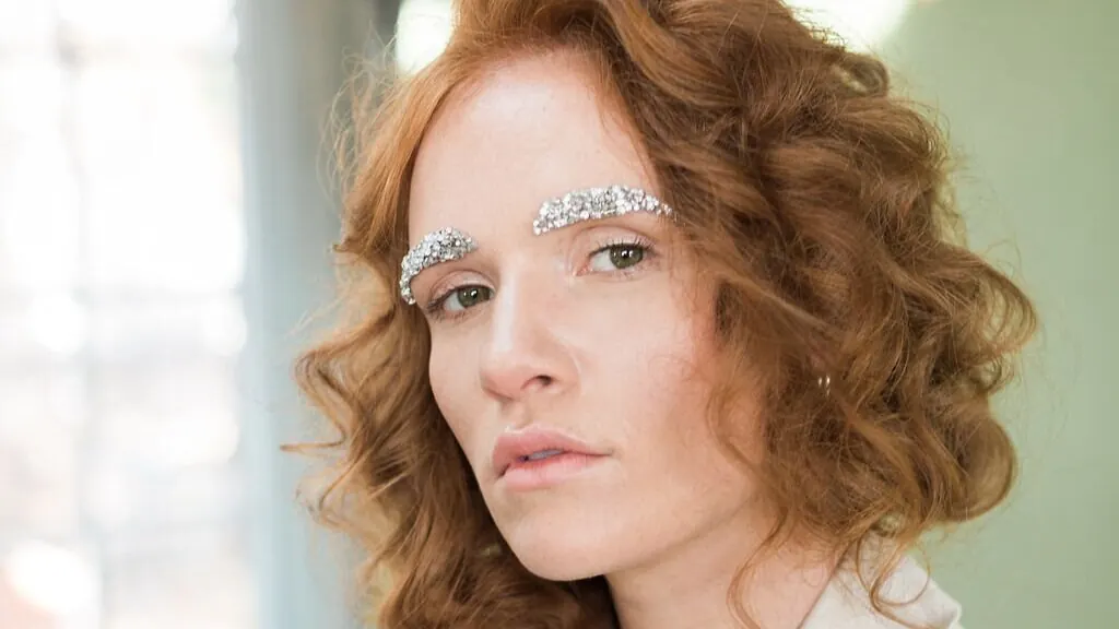 Woman with curly red hair and silver rhinestones on her eyebrows