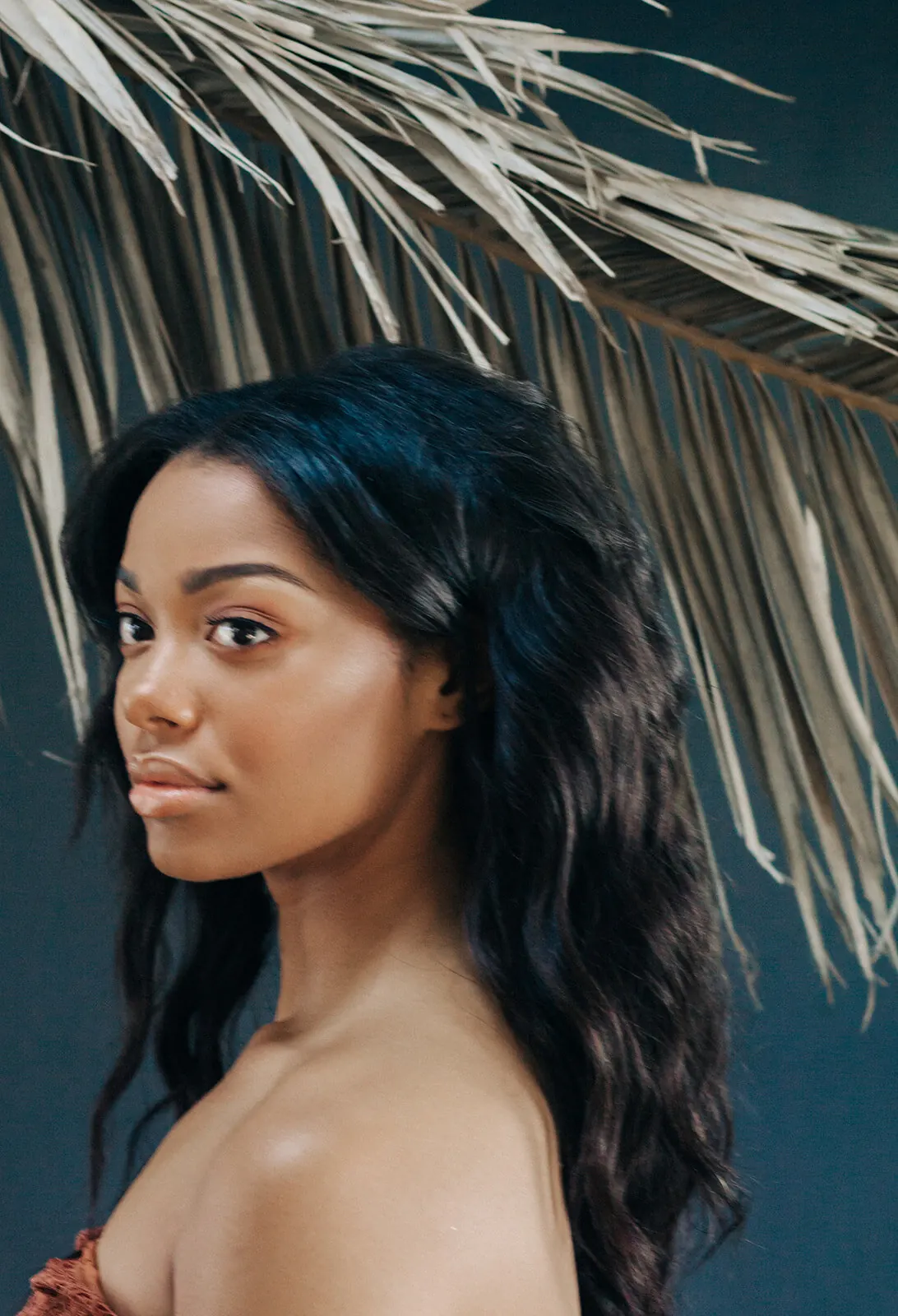 Woman with long dark curls and glowing skin beneath palm fronds