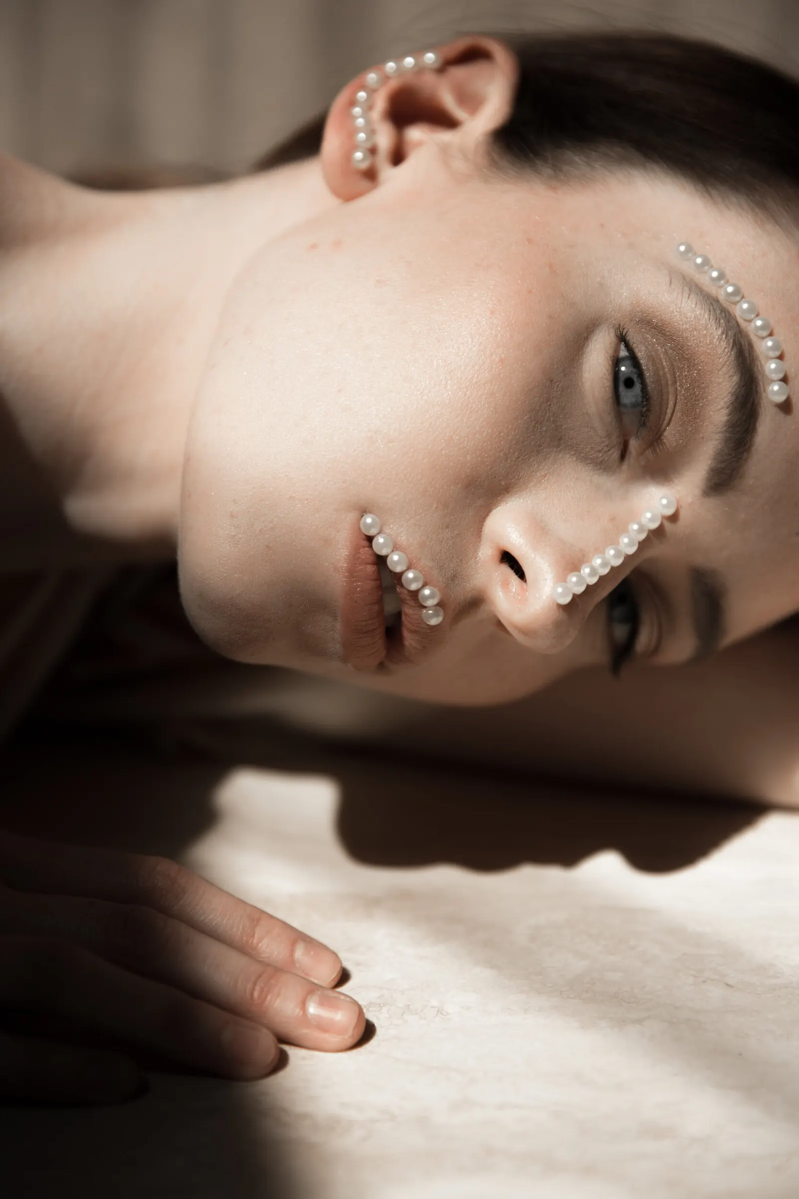 Woman resting on a table with pearl accents placed along her cheekbone