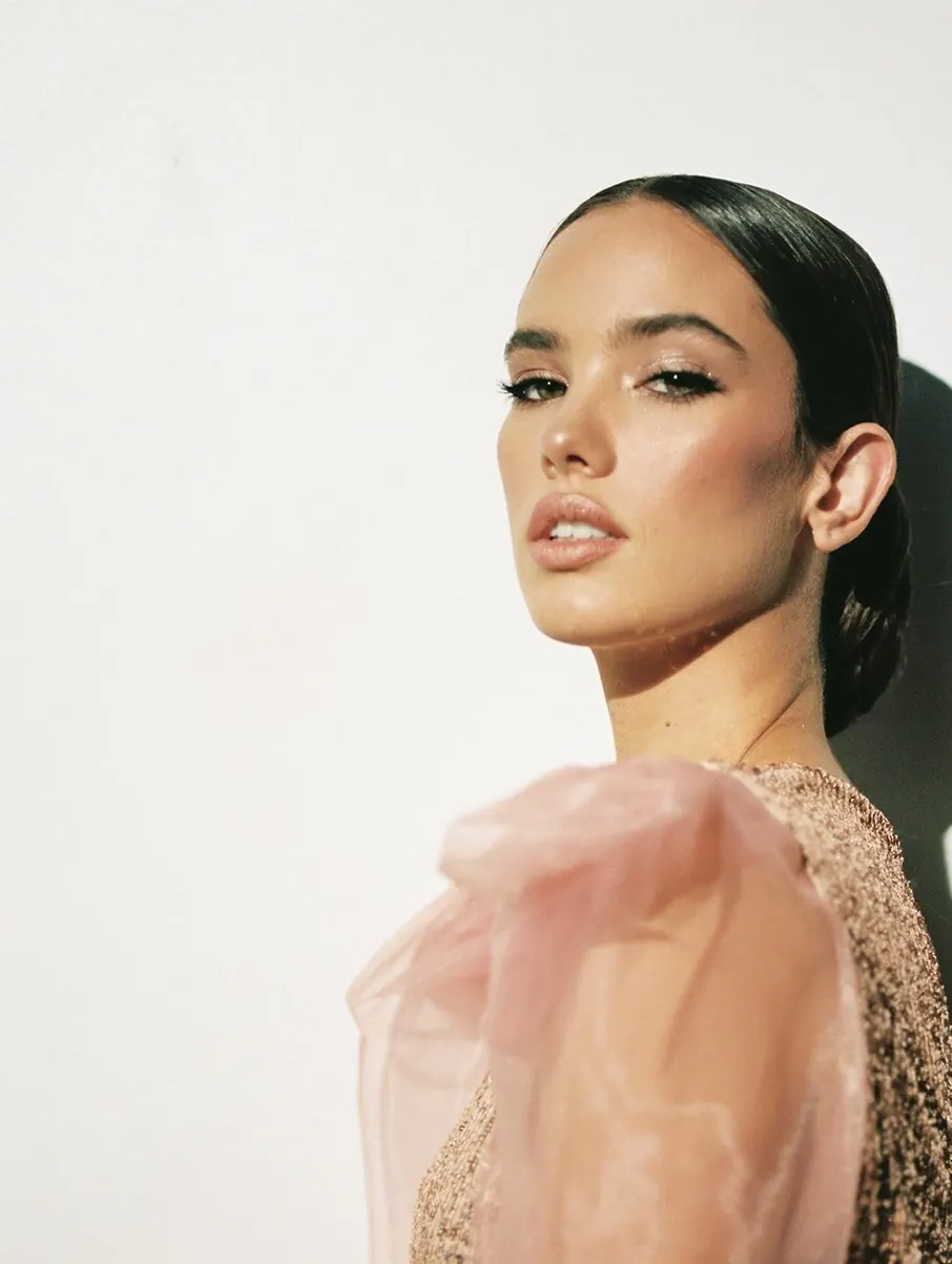 Woman with sleek dark hair, defined brows and a sheer blush-pink sleeve